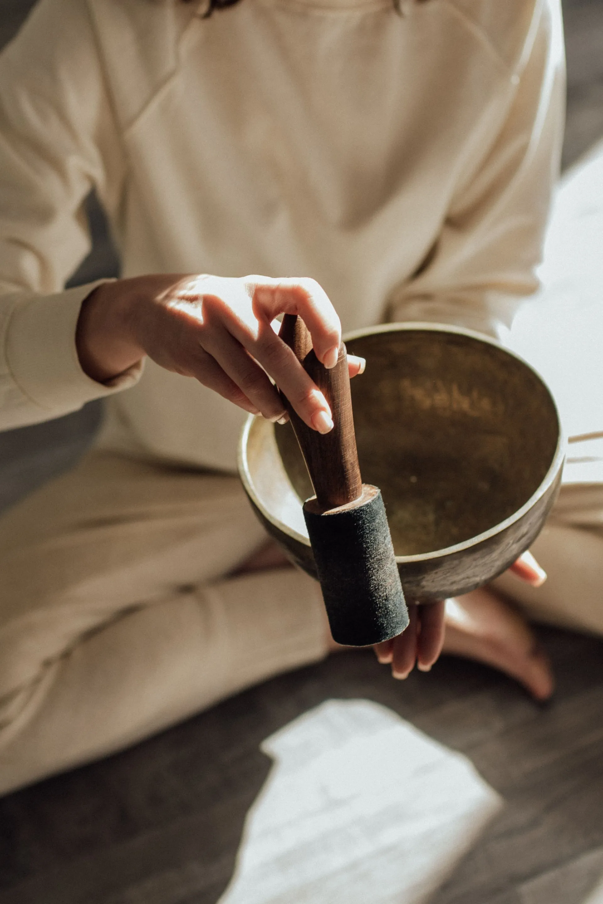 Hands playing a brass singing bowl with a wooden mallet